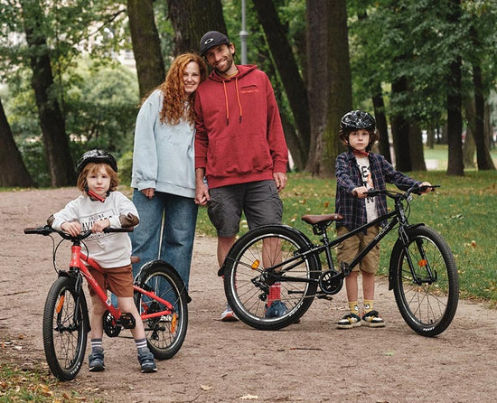 Dos chicos con casco junto a sus bicicletas SHULZ en un parque, acompañados por sus padres